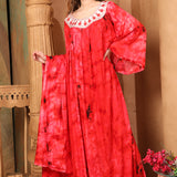 A woman standing in a beautifully colored red kaftan with black and white thread work, posing against a backdrop with furniture.