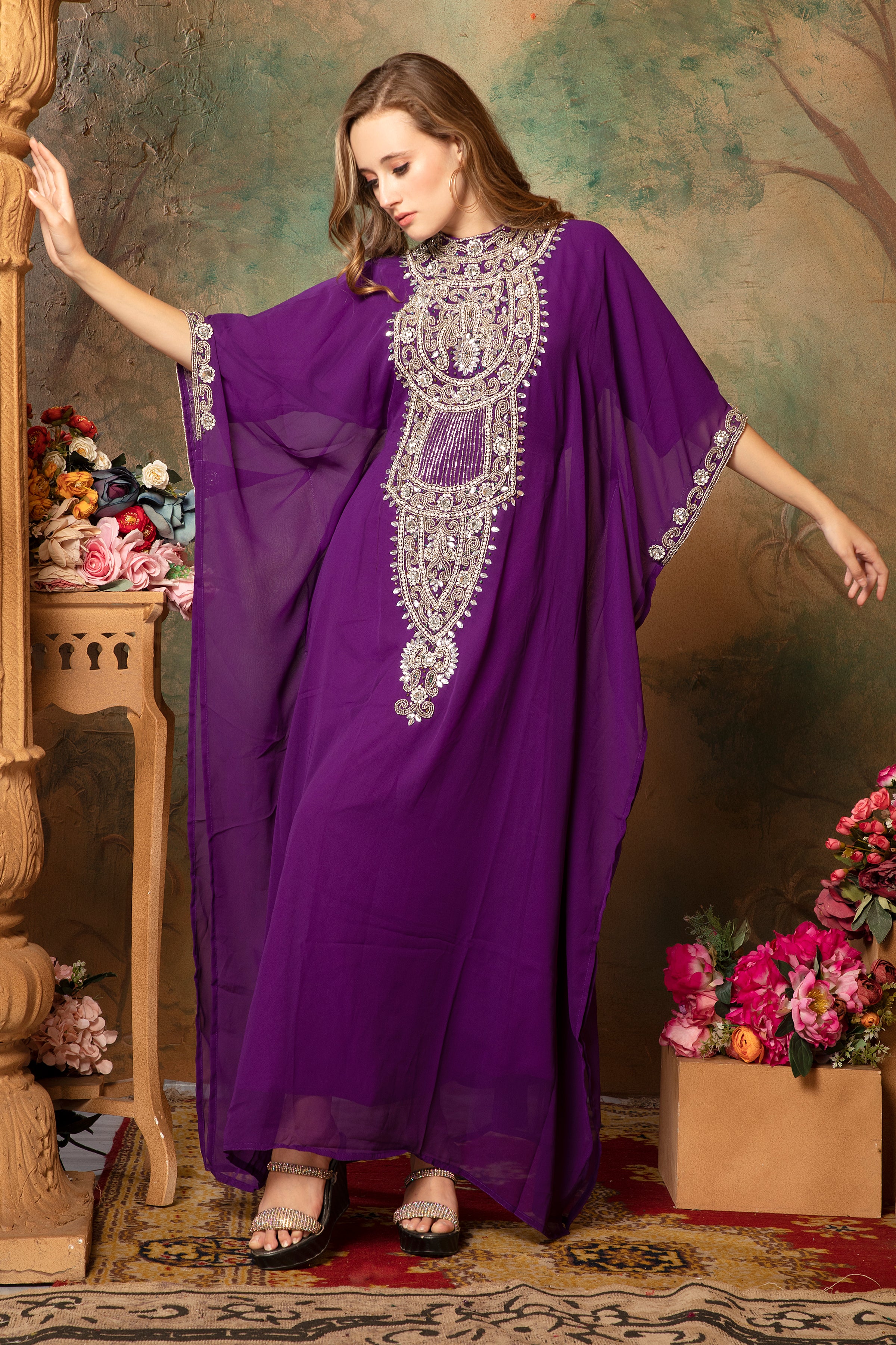A woman wearing a purple farasha kaftan with embroidered silver beads, posing in a floral backdrop.