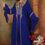 A woman standing in a beautiful blue caftan with golden bead embellishments, posing in a traditional, elegant style.