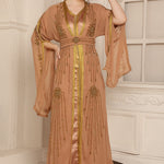 A woman wearing a beige and gold Moroccan caftan with long sleeves and embellishments.