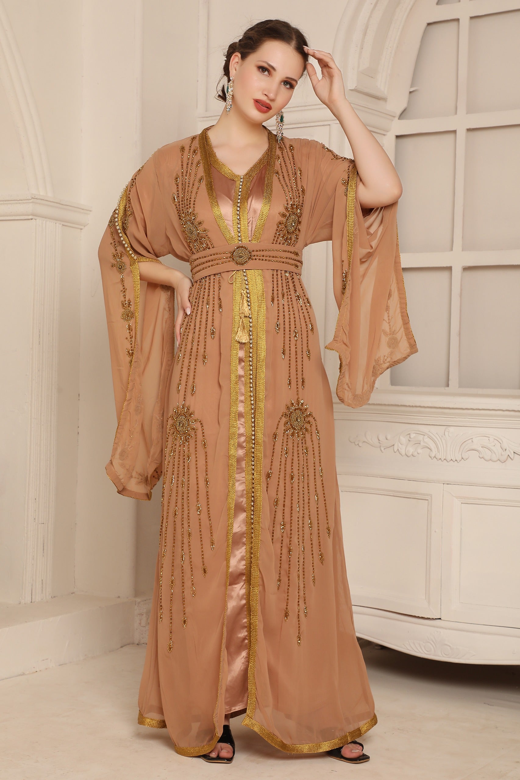 A woman wearing a beige and gold Moroccan caftan with long sleeves and embellishments.
