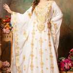 A woman modeling a white abaya dress with golden bead embellishments and a floral pattern. The dress has long straight sleeves and is lined from the inside.