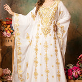 A woman modeling a white abaya dress with golden bead embellishments and a floral pattern. The dress has long straight sleeves and is lined from the inside.