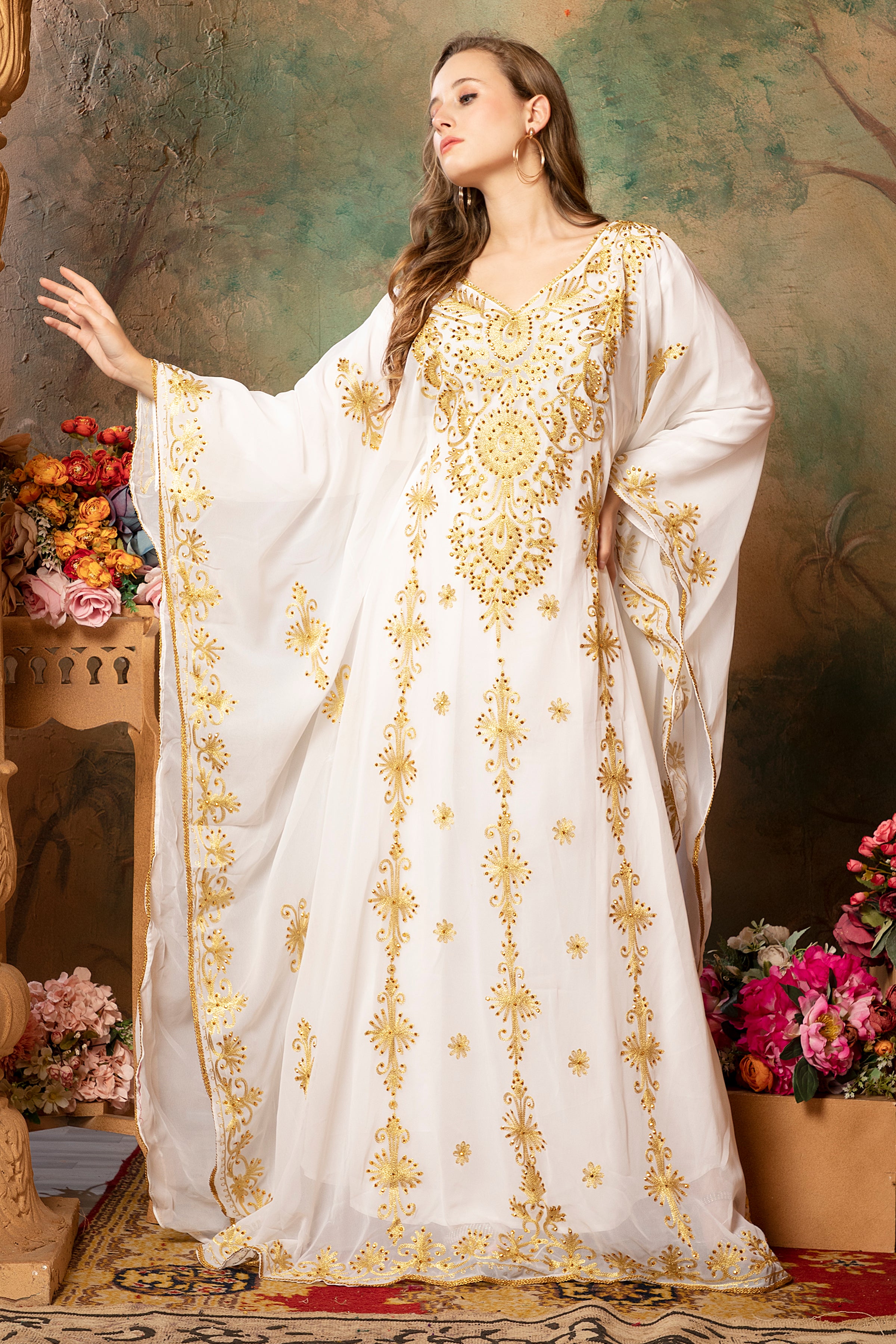 A woman modeling a white abaya dress with golden bead embellishments and a floral pattern. The dress has long straight sleeves and is lined from the inside.