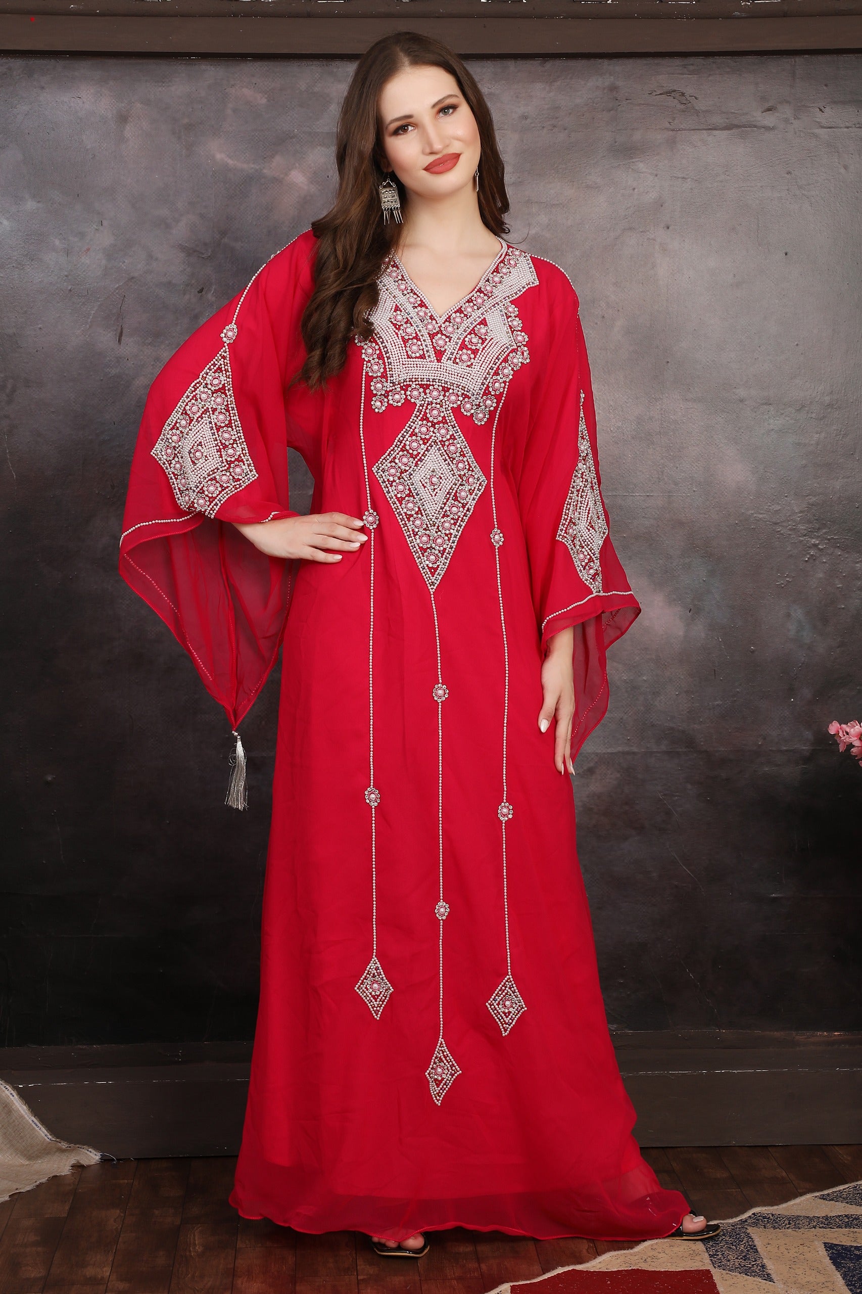 A woman wearing a red long sleeve caftan with silver color bead embellishments. The caftan has a straight cut and appears to be made of polyester georgette fabric.