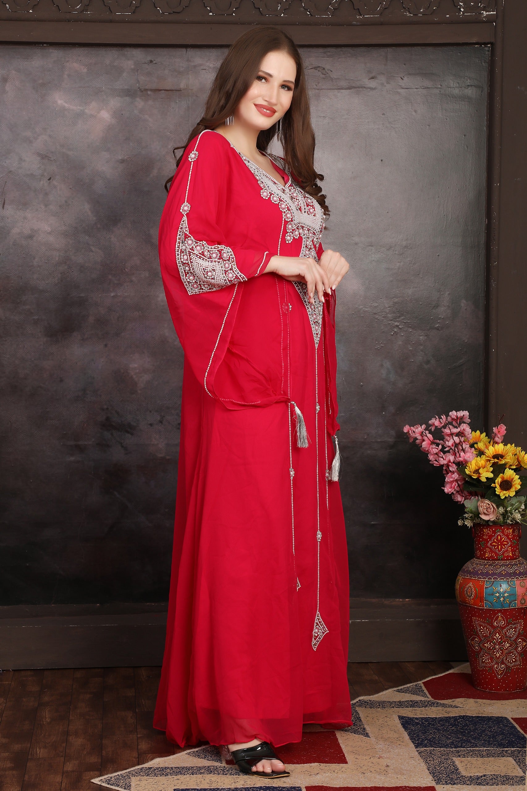Woman in a red dress with silver embellishments standing against a dark background.