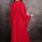 Woman wearing a red dress with embroidered sleeves against a textured wall.
