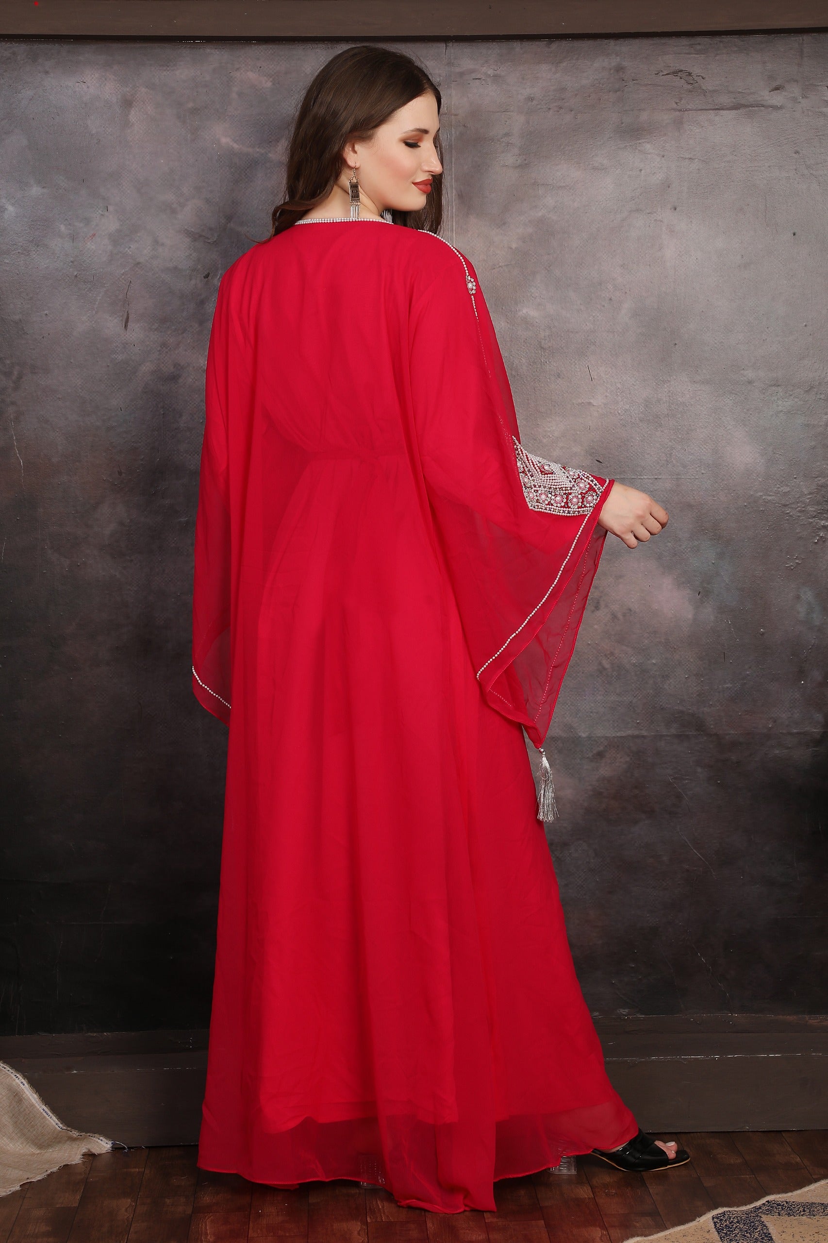 Woman wearing a red dress with embroidered sleeves against a textured wall.