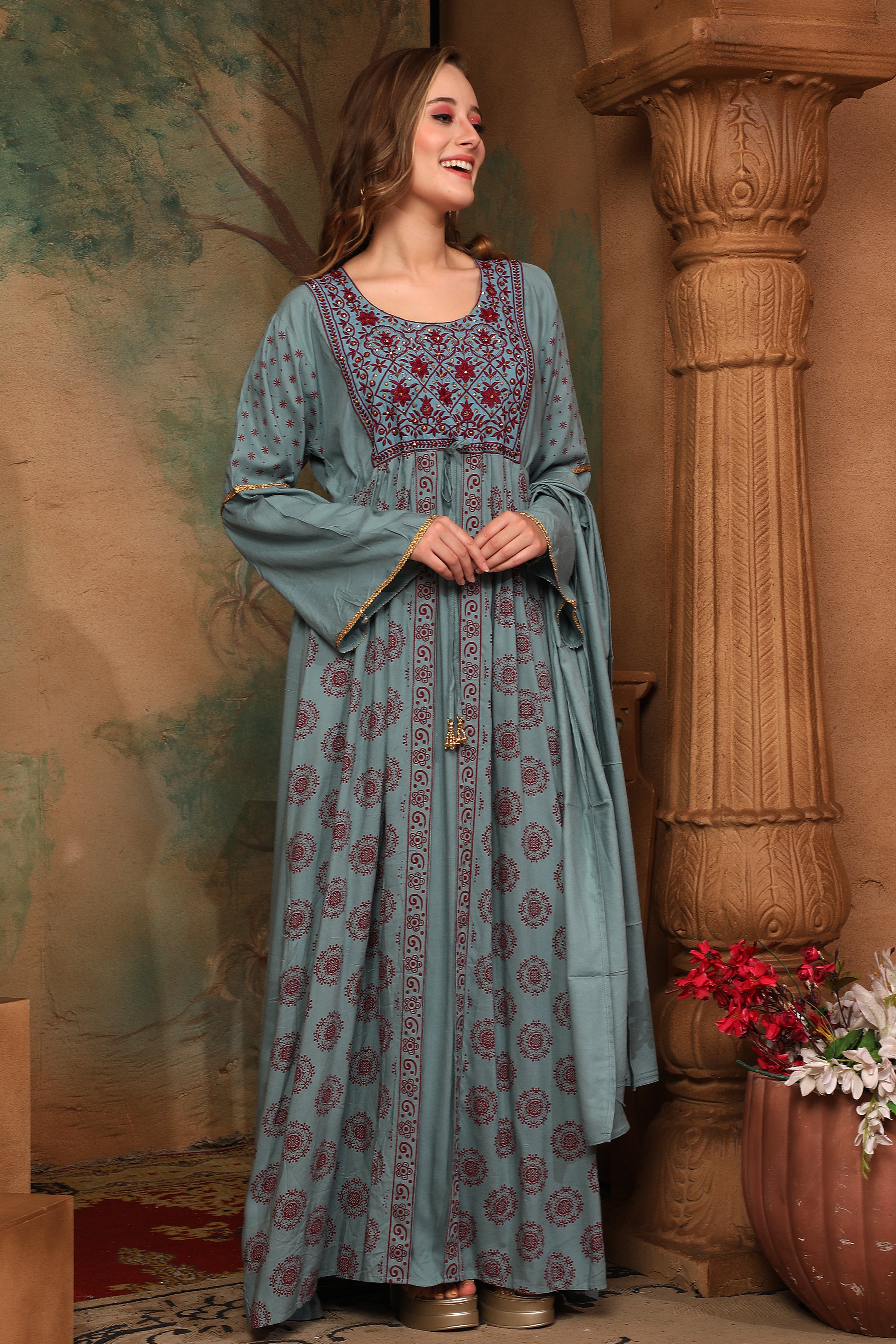 A woman standing in a beautiful traditional blue cotton kaftan with floral patterns, featuring long sleeves and a maxi length.
