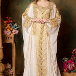 A woman wearing a traditional white and gold abaya dress with embroidered details, posing in a floral backdrop.