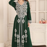 A woman wearing a green Moroccan caftan with silver embellishments. The caftan has a straight long sleeve design and comes with an additional belt.