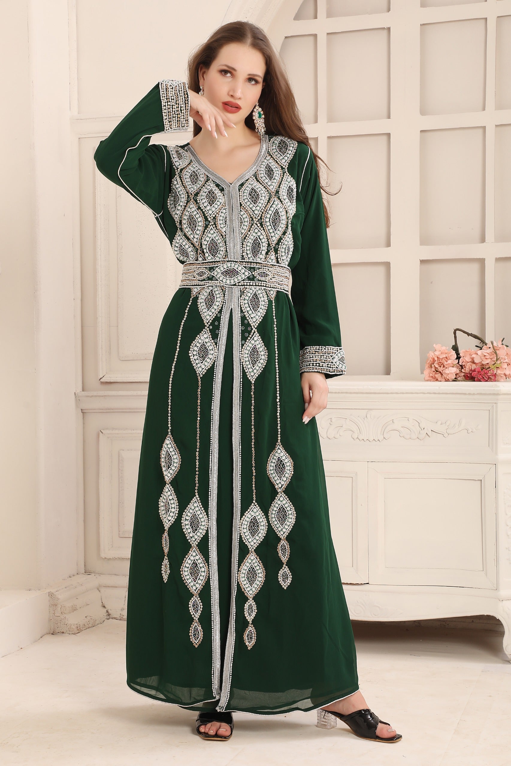 A woman wearing a green Moroccan caftan with silver embellishments. The caftan has a straight long sleeve design and comes with an additional belt.