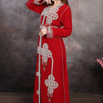 Woman wearing a red embroidered dress against a textured wall.