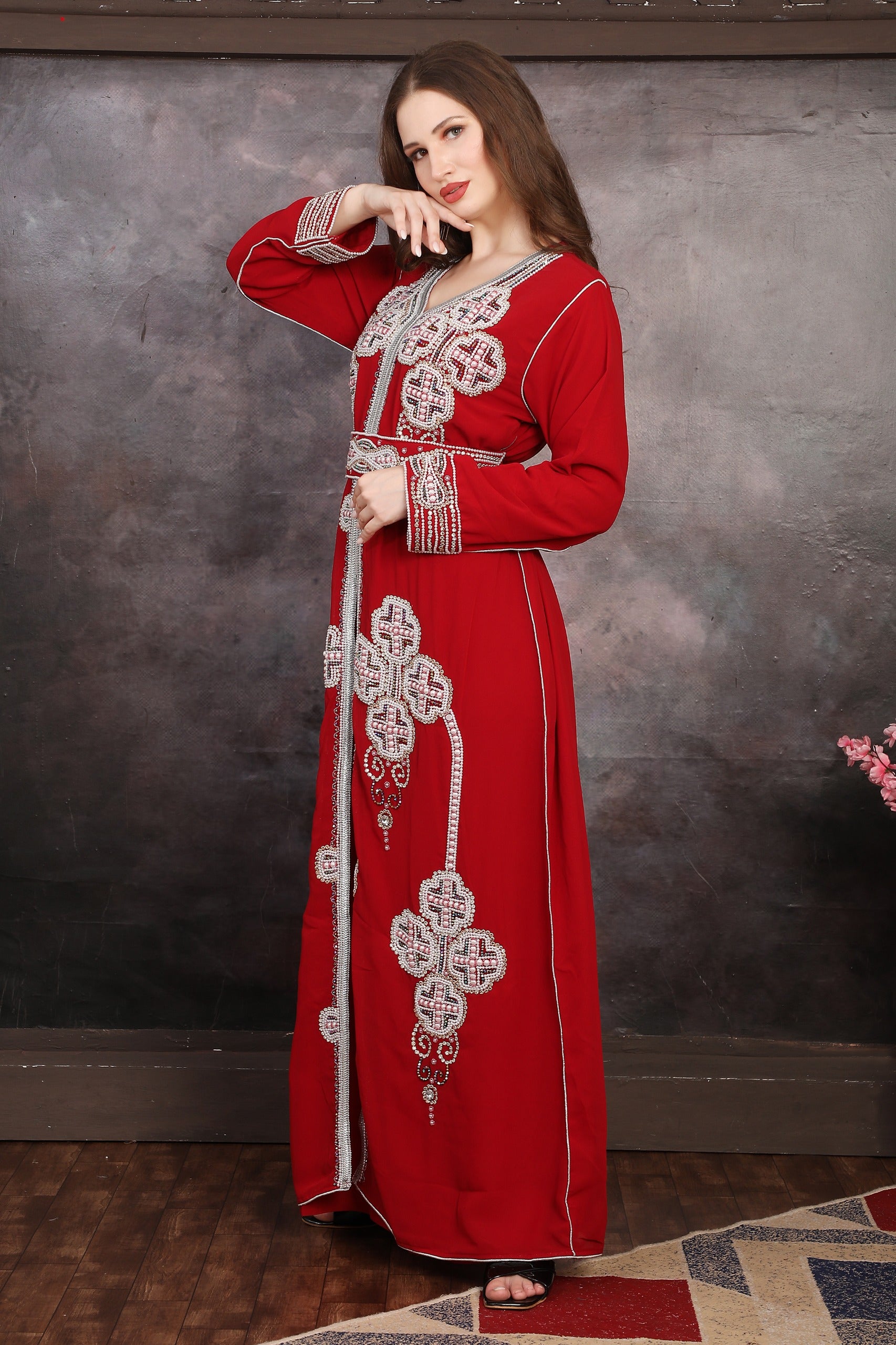 Woman wearing a red embroidered dress against a textured wall.