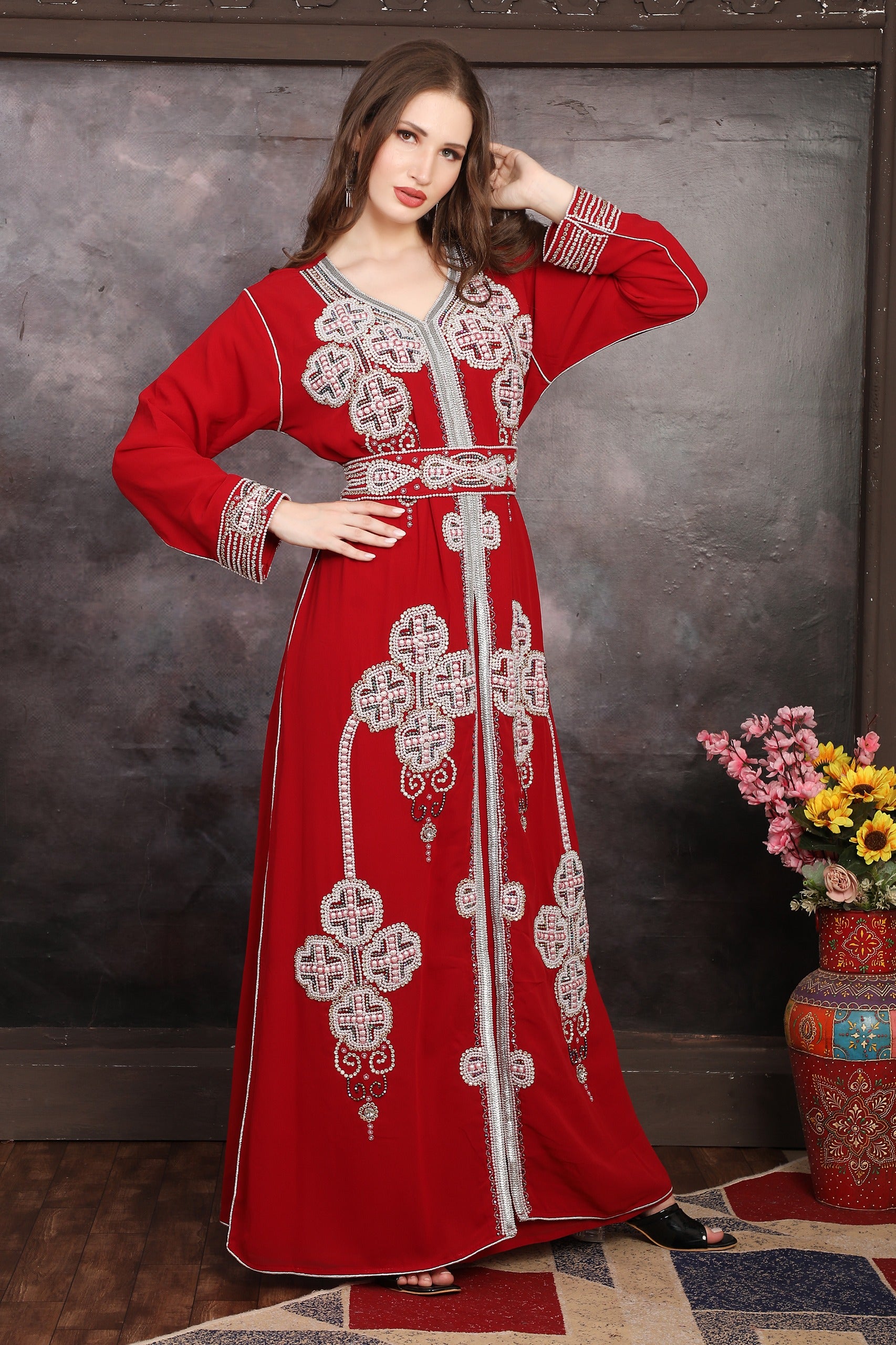 Woman in a red embroidered dress with a vase of flowers on a wooden table.