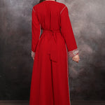 Back Side Woman wearing a red dress with silver trim against a textured wall.