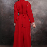 Back Side Woman wearing a red dress with silver trim against a textured wall.