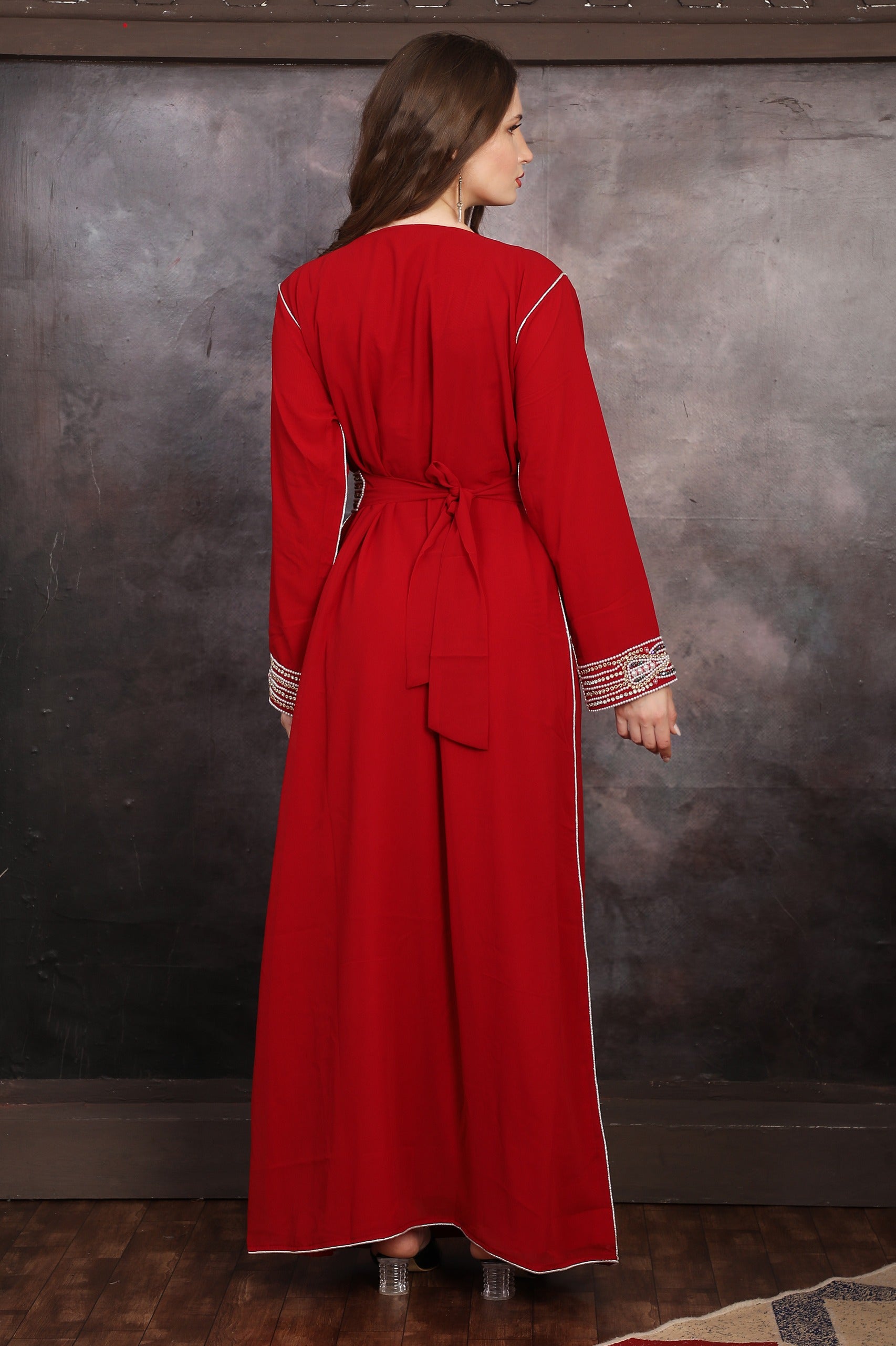 Back Side Woman wearing a red dress with silver trim against a textured wall.