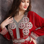 Close-up of a Woman wearing a red embroidered dress against a textured wall.