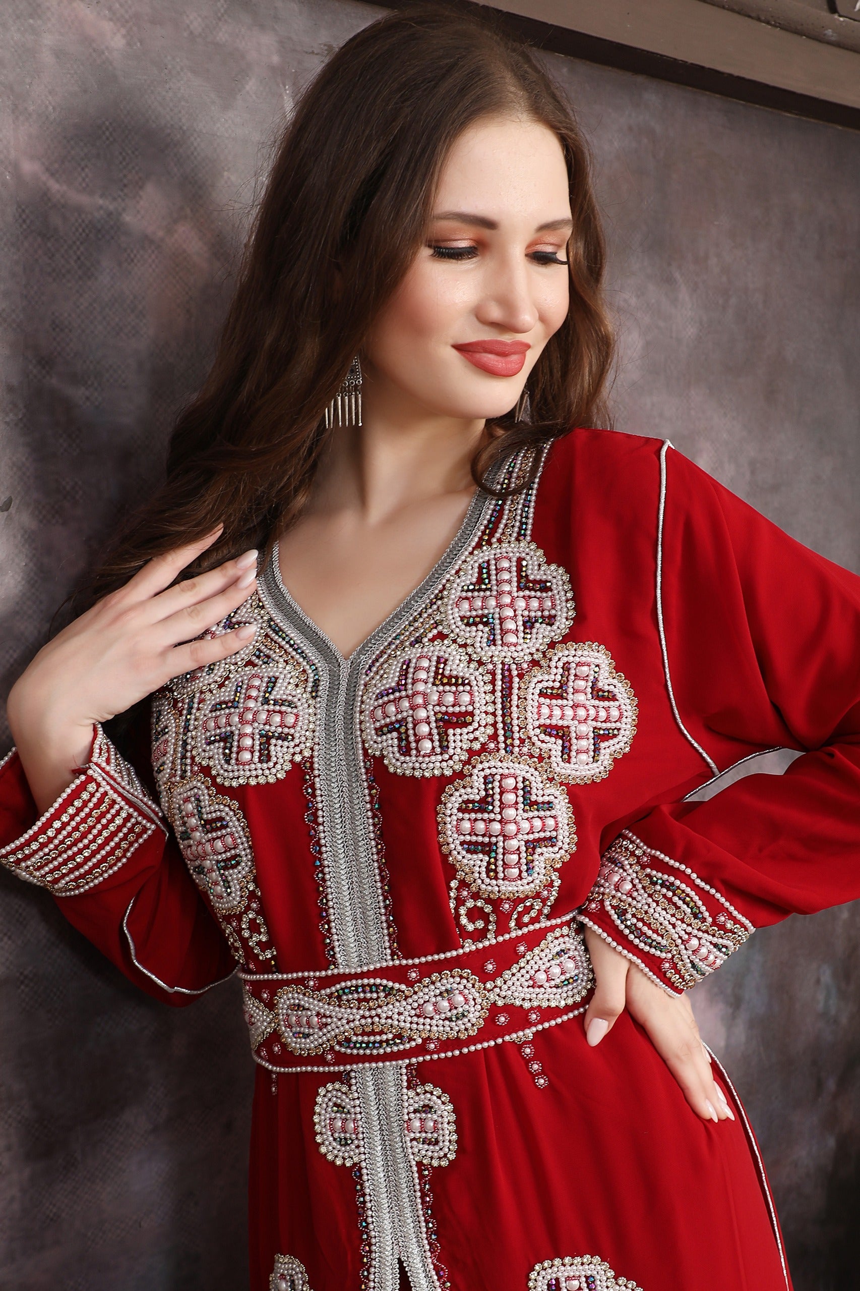 Close-up of a Woman wearing a red embroidered dress against a textured wall.