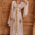 A woman wearing a beige and gold Moroccan caftan with long sleeves and embellishments.