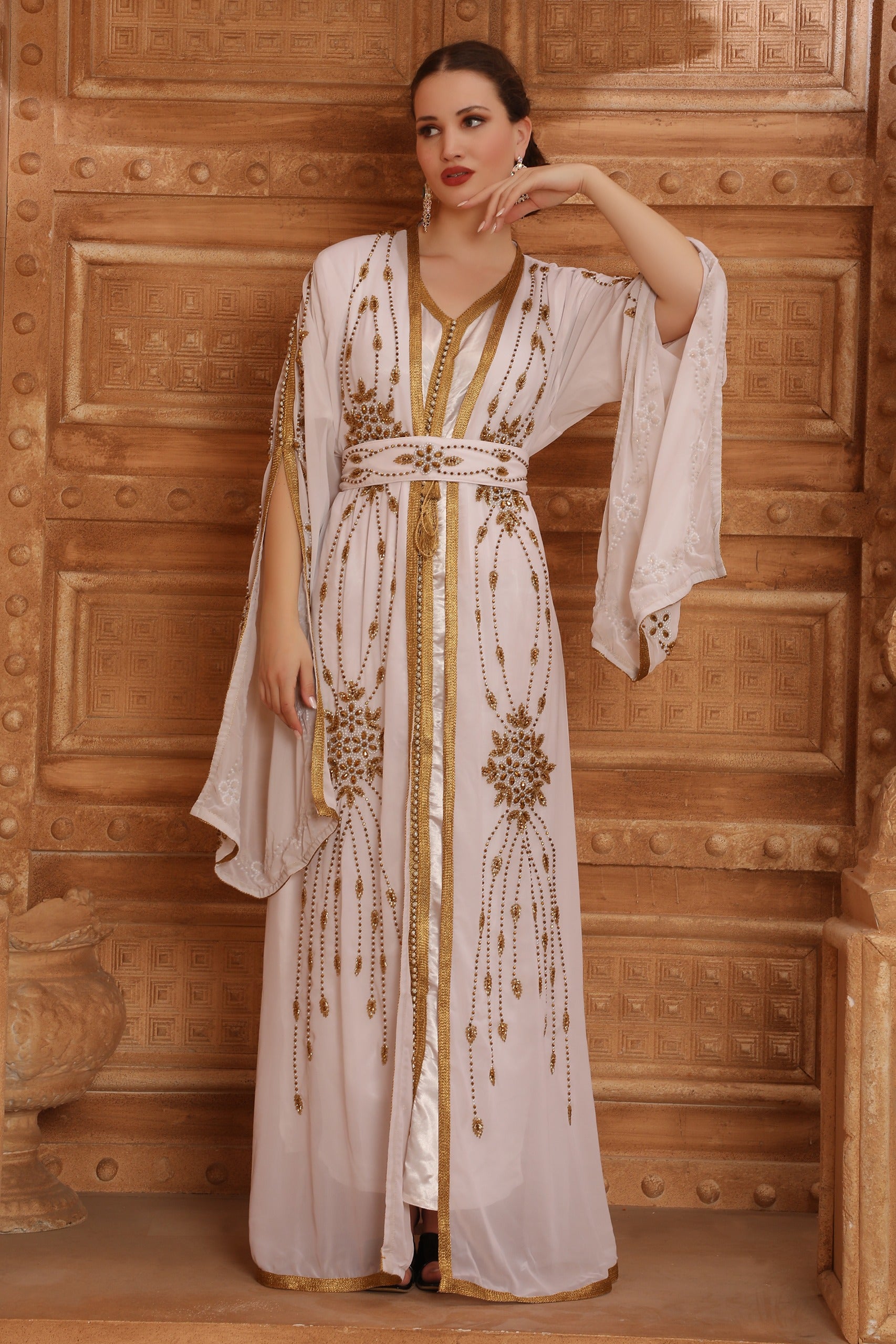 A woman wearing a beige and gold Moroccan caftan with long sleeves and embellishments.