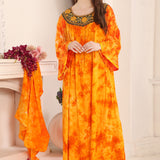 A woman standing in a room wearing a yellow and orange floral kaftan with gold bead detailing around the neckline.