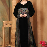 A woman standing in a beautifully embroidered black velvet gown with long straight sleeves, posing in a room with elegant decor.